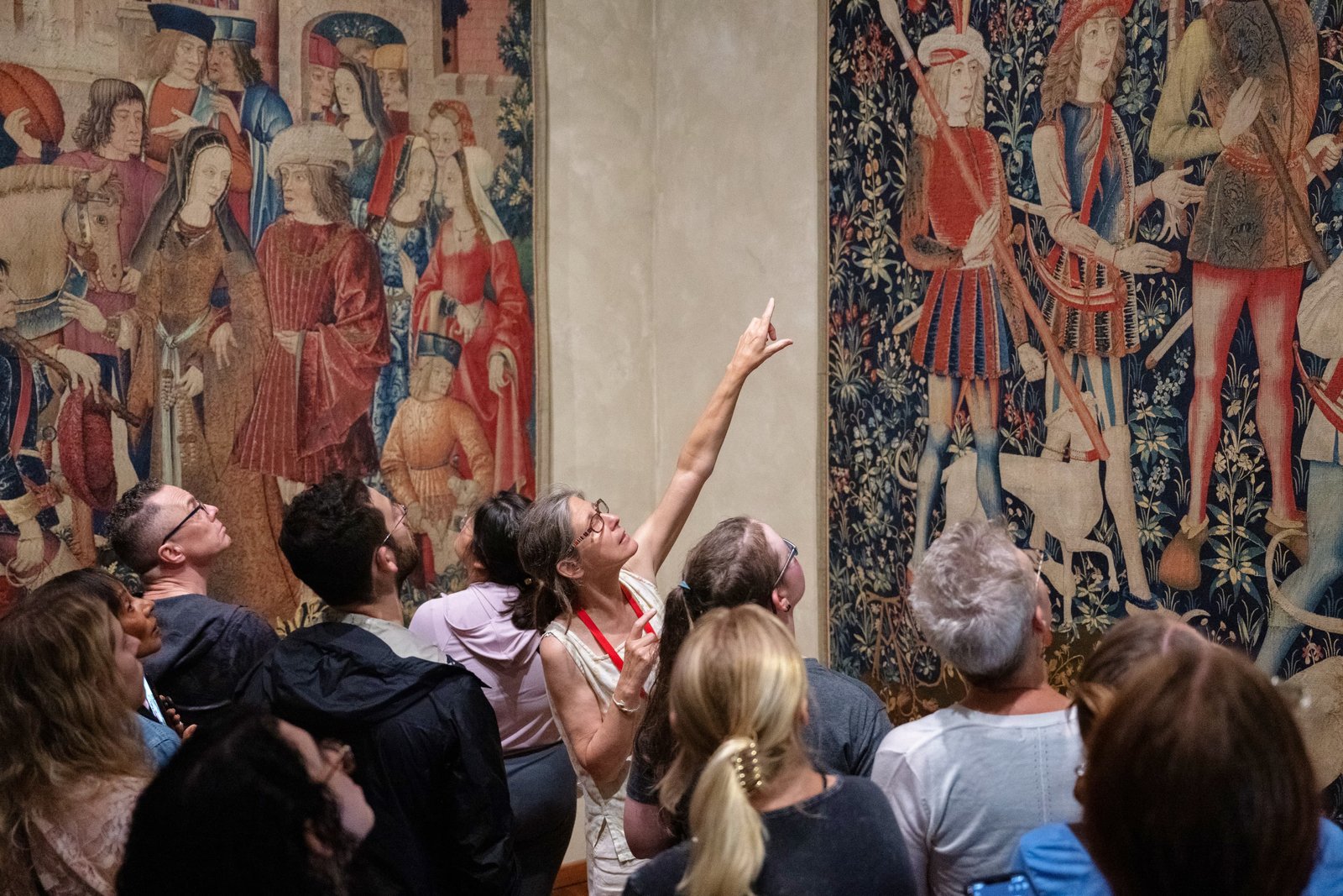 A speaker pointing out a detail to a group of people in a gallery looking at tapestries.